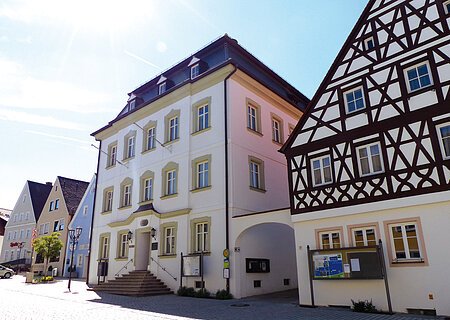 Straßenansicht der Monheimer Innenstadt: Im Vordergrund das Rathaus der Stadt Monheim, mit weiteren mehreren Gebäuden, darunter ein Fachwerkhaus, das man Schindlerhaus nennt.