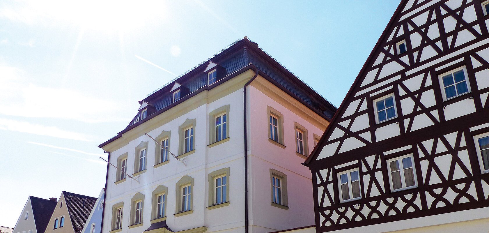 Straßenansicht der Monheimer Innenstadt: Im Vordergrund das Rathaus der Stadt Monheim, mit weiteren mehreren Gebäuden, darunter ein Fachwerkhaus, das man Schindlerhaus nennt.