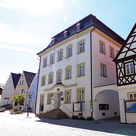Straßenansicht der Monheimer Innenstadt: Im Vordergrund das Rathaus der Stadt Monheim, mit weiteren mehreren Gebäuden, darunter ein Fachwerkhaus, das man Schindlerhaus nennt.
