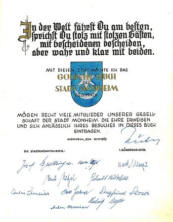 Erster Eintrag im Goldenen Buch der Stadt Monheim: Oben ein Zitat, darunter das Wappen der Stadt Monheim in blau. Darunter ein weiterer Text, datiert mit 10.11.1969, mit etlichen Unterschriften darunter.