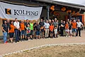 Gruppenfoto von ca. 30 Personen vor einem Gebäude auf einem gepflastertem Platz mit einem großen Kolping-Banner und orangen Luftballons. Im Vordergrund eine Rasenfläche.