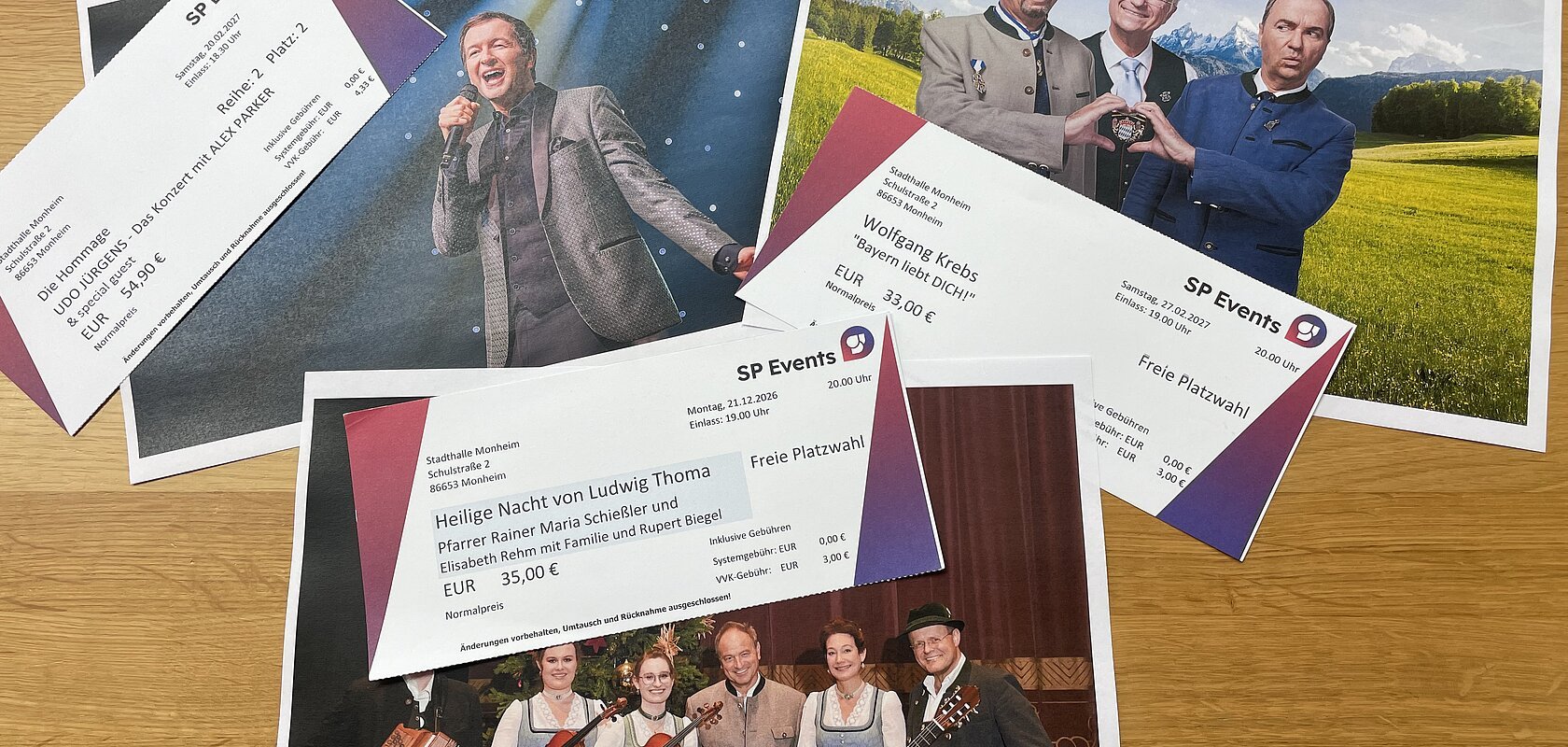 Drei Konzertkarten von SP Events liegen auf Fotos von Musikern in traditioneller und moderner Kleidung auf einem Holztisch. Kartenvorverkauf für die nächsten Veranstaltungen in Monheim