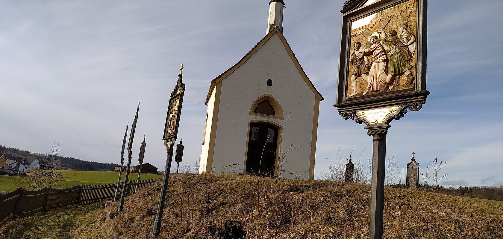 Kleine weiße Kapelle, die Kalvarienbergkapelle in Wittesheim, auf einem Hügel mit mehreren Kreuzwegstationen entlang eines Weges im Vordergrund.