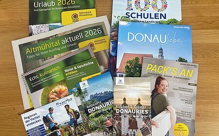 Mehrere Broschüren und Flyer zu Urlaub, Naturpark Altmühltal und Donau-Ries auf Holztisch liegend. Neuauflagen verschiedener Flyer und Broschüren in der Tourist-Information zur Abholung