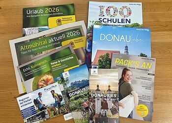 Mehrere Broschüren und Flyer zu Urlaub, Naturpark Altmühltal und Donau-Ries auf Holztisch liegend. Neuauflagen verschiedener Flyer und Broschüren in der Tourist-Information zur Abholung