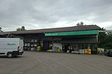 Außenansicht eines BayWa Agrar Gebäudes mit geparktem weißen Lieferwagen und Paletten mit Agrarprodukten davor.