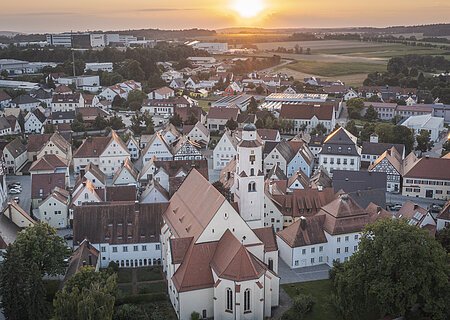 Luftaufnahme einer Kleinstadt mit Kirche und Fachwerkhäusern bei Sonnenuntergang, Felder im Hintergrund.