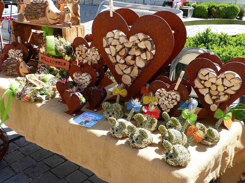 Marktstand mit Holzherzen, Holztieren und dekorativen Figuren aus Stroh auf einem mit Leinen bedeckten Tisch.