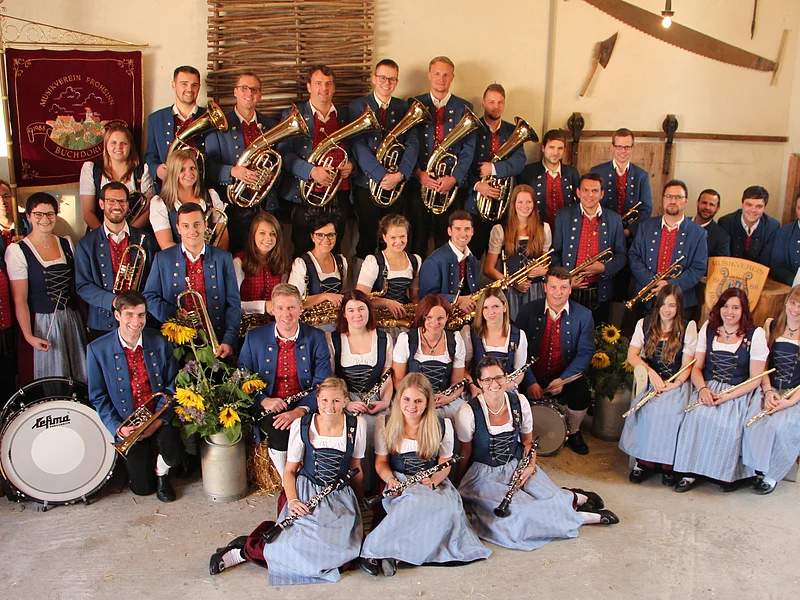 Gruppe von Menschen eines Musikvereins in traditioneller Kleidung mit Musikinstrumenten in einem Raum.
