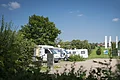 Wohnmobilstellplatz Monheim Wohnmobile parken auf einem Stellplatz, umgeben von Bäumen und Wiesen unter blauem Himmel.