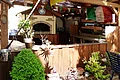 Pizzeria Ristorante Romana - unser Holzofen im Freien Außenküche mit Holztheke, Pizzaofen, italienischer Flagge und Pflanzen im Gartenbereich. Recht im Bild ein grauer Stuhl zu sehen.