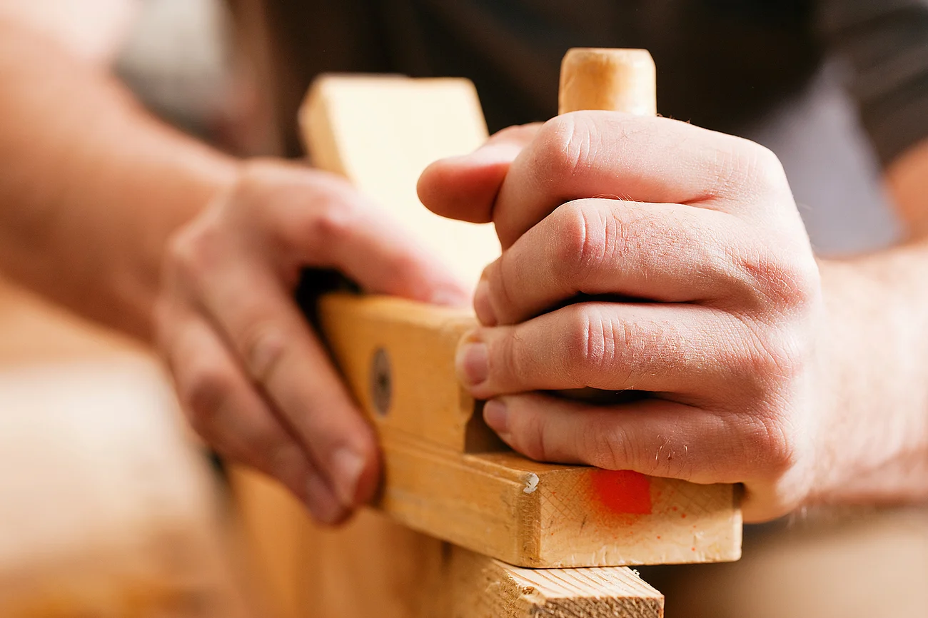 Gewerbebetriebe Hände halten eine Hobelmaschine und bearbeiten ein Stück Holz in Nahaufnahme.