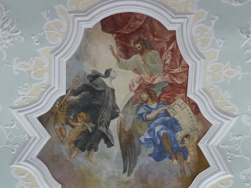 Stadtpfarrkirche St. Walburga Monheim - Deckengemälde Deckenfresko mit religiösen Figuren, darunter Engel und Heilige, die über einer Landschaft mit Gebäuden, der Stadt Monheim schweben.