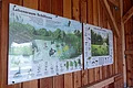Fischereilehrhütte Monheim - mit Informationen zum Lebensraum Weiher Zwei Infotafeln zu Pflanzen und Tieren der Schilfzone und eines Weihers an einer Holzwand in einem Unterstand.