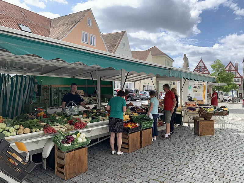 Wochenmarkt Monheim Marktstand des Wochenmarkts in Monheim mit Obst und Gemüse in der Auslage auf dem gepflastertem Marktplatz. Mehrere Personen kaufen dort ein. Fachwerkhäuser im Hintergrund und bewölkter Himmel.