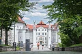 Eingangstor eines historischen Gebäudes mit Statuen und Bäumen im Vordergrund.