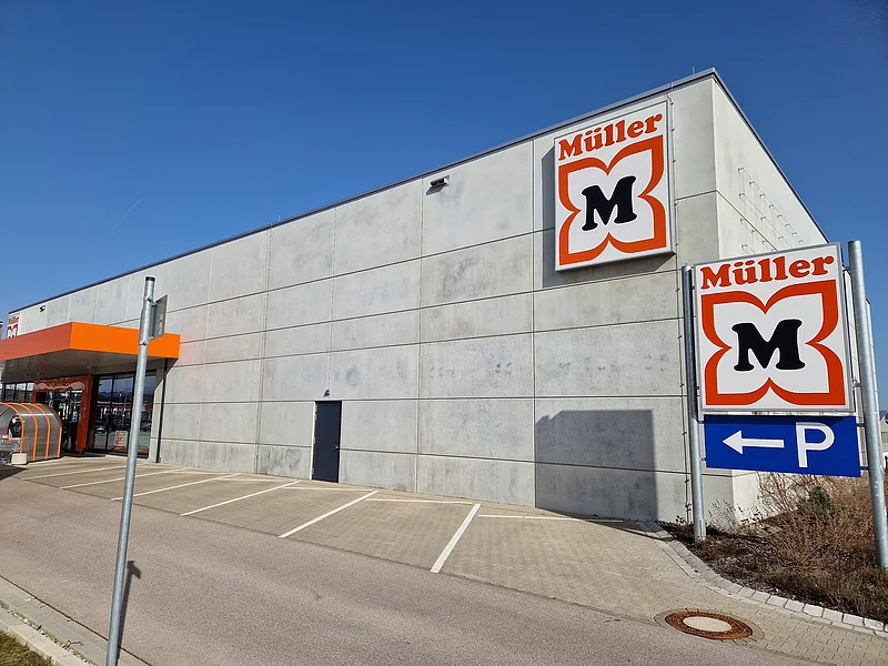 Drogeriemarkt Müller - Parkflächen direkt am Markt Außenansicht eines Müller-Marktes mit Parkplätzen und blauem Himmel.