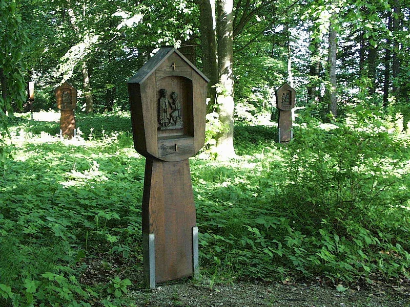 Holztafeln auf einem Kreuzweg mit religiösen Schnitzereien in einem bewaldeten Gebiet.