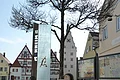 Buchstabenweg M-O-N-H-E-I-M Im Vordergrund ein großer grauer Buchstabe "O" aus Stein mit einer Infotafel daneben auf einem gepflasterten Platz. Dahinter, rechts im Bild zwei weitere Informationsvitrinen der Stadt Monheim, umgeben von historischen Gebäuden im Hintergrund. Der Buchstabe ist ein Teil des Monheimer Buchstabenweges.
