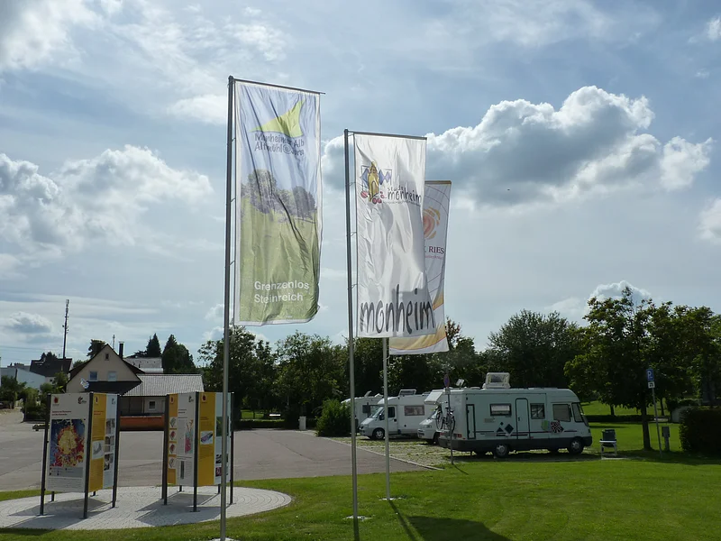 Wohnmobilstellplatz mit Geopark Infostelle Monheim Die Geopark Infostelle mit Flaggen und im Hintergrund die Wohnmobile auf dem Wohnmobilstellplatz in Monheim.