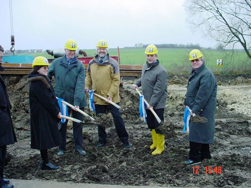 Spatenstich für die neue Kläranlage der Stadt Monheim am 12.12.2001 Fünf Personen mit gelben Helmen und Schaufeln stehen auf einer Baustelle mit Erde und Wiese im Hintergrund bei bewölktem Himmel.