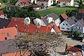 Drei Störche stehen in einem großen Nest auf einem Dach, im Hintergrund Sicht auf Häuser einer Stadt mit roten und braunen Dächern.