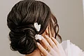 Laura Burlefinger - Make-up Artist & Hairstylist Monheim Frau mit hochgestecktem Haar und weißen Blüten, Hand berührt Gesicht, weißes Tüllkleid mit Perlendetails
