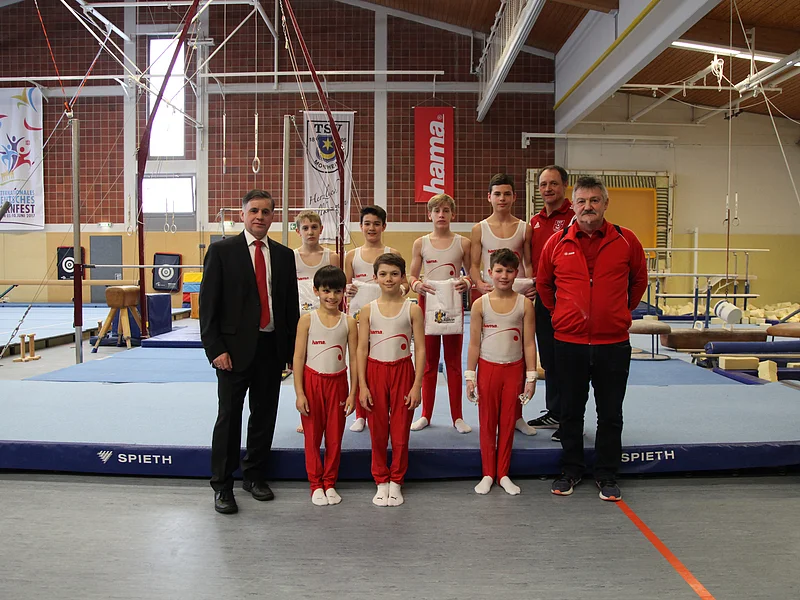 Jubiläumsveranstaltung "25 Jahre Stadthalle Monheim" - der TSV Monheim zeigte sein Können in den Sparten Turnen, Karate und Sportakrobatik Gruppenfoto mit sieben Jungen in Turnkleidung, zwei Männern in Sportkleidung rechts von ihnen und einem Mann im Anzug links, in einer Turnhalle auf blauer Matte vor Turngeräten.