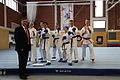 Jubiläumsveranstaltung "25 Jahre Stadthalle Monheim" - der TSV Monheim zeigte sein Können in den Sparten Turnen, Karate und Sportakrobatik Gruppe von sieben Karatekämpfern in weißen Anzügen, teilweise mit blauen Handschuhen auf blauer Matte und einem Mann im Anzug links von der Gruppe, in einer Sporthalle. Im Hintergrund ein Banner und weitere Sportgeräte.
