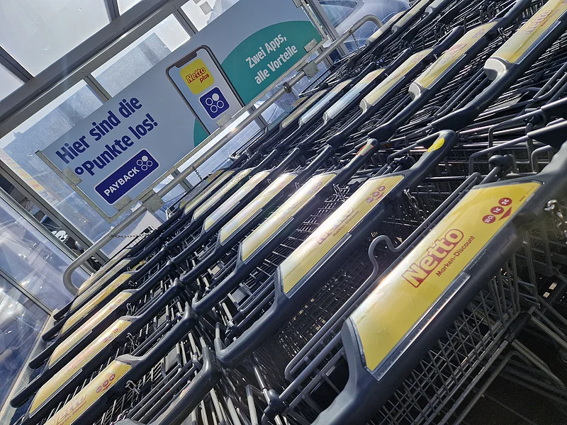 Eingeschobene Einkaufswagen mit Netto-Logo vor Werbetafel für PAYBACK-Punkte und zwei Apps.