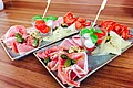 Essensangebot bei der Pizzeria Va Bene in Monheim Zwei gleich angerichtete Teller mit Aufschnitt, Käse, Schinken, Tomaten, Mozzarella und Basilikum auf Holzoberfläche.