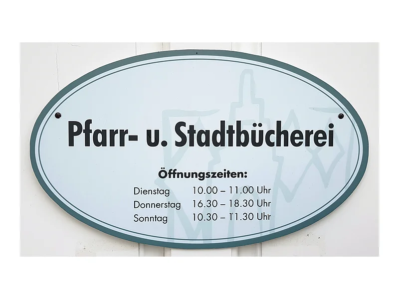 Schild mit Öffnungszeiten der Pfarr- und Stadtbücherei, Dienstag 10-11 Uhr, Donnerstag 16:30-18:30 Uhr, Sonntag 10:30-11:30 Uhr.