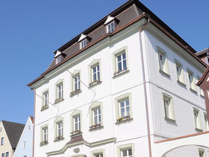 Das Rathaus der Stadt Monheim, am Marktplatz. Ein weißes, dreistöckiges Gebäude mit Satteldach und mehreren Fenstern, im Vordergrund gepflasterter Marktplatz.