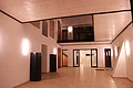 Kreuzwirt "Haus der Kultur" Monheim Beleuchteter heller Innenraum mit heller Holzdecke, weißen Wänden, zwei schwarzen Säulen links an der Wand, einer mit Holz verkleideten Treppe und mehreren Türen und Fenstern. Heller Bodenbelag aus Fließen.