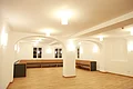 Kreuzwirt "Haus der Kultur" Monheim Großer leerstehender heller Raum mit hellem Holzfußboden, weißen Wänden, Holzbänken hinten entlang der Wände, mehreren Deckenlampen und Rundbögen in der Mitte des Raums.