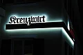 Kreuzwirt "Haus der Kultur" Monheim Zwei weiß beleuchtete dunkelrote Schriftzüge „Kreuzwirt“ an einer helle Hauswand bei Nacht um die Ecke verbunden mit einem dunkelrotem Balken darunter.