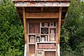Wildbienennisthilfe am Lehrbienenstand Monheim Holzgestell mit Ziegeln und Holzblöcken, als Insektenhotel gestaltet. Die Wildbienennisthilfe in Monheim steht auf einer Wiese vor Büschen. Unter dem Holzgestell liegen große weiße Steine.