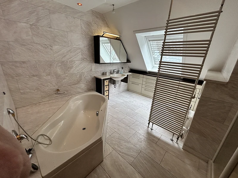 Miet-Maisonette am Marktplatz - Badezimmer im Obergeschoss Miet-Maisonette. Badezimmer mit Badewanne, Waschbecken, Spiegelschrank, Dachfenster und Heizkörper vor Fliesenwand und -boden.