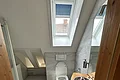 Miet-Maisonette am Marktplatz - Dusche/WC im Dachgeschoss Badezimmer mit Dachfenster, Toilette, Dusche, Waschbecken mit Holzplatte und Spiegel, graue Fliesenboden und Wände.