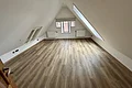 Miet-Maisonette - Wohn-/Schlafraum im Dachgeschoss Leerer Raum mit schrägen Wänden, Holzfußboden, drei Fenstern und zwei Heizkörpern unter dem Fenster.