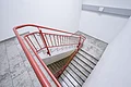 Appl Bürogebäude Innenaufnahme 7 Treppenhaus mit grauen gefliesten Stufen und rotem Handlauf aus Metall, weiße Wände, Blick von oben.