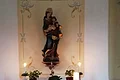 Die Marienstatue in der Kalvarienbergkapelle in Wittesheim - gestiftet anlässlich eines Jahrgangstreffens Altar mit Statue der Marienstatue, Kerzen auf dem Altar, sowie Blumen und Pflanzen in einem kleinen Raum einer Kapelle.