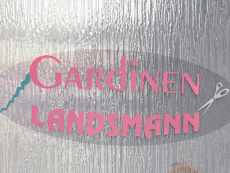 Gardinen Landsmann - Logo Aufgeklebtes Logo mit Schriftzug „Gardinen Landsmann“ in pink hinter einer strukturierten Glasfläche mit silberner Schere rechts neben dem Schriftzug und einem Zickzack-Motiv in türkis links neben dem Schriftzug.
