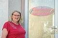 Gardinen Landsmann - Manuela Landsmann Frau mit rotem Shirt und Brille steht vor einer Glastür mit der Aufschrift „Gardinen Landsmann“ und einem Scherensymbol.