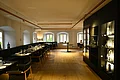 Restaurant im Hotel by Ferber - Hotel, Steakhouse, Bar in der historischen Altstadt von Monheim Innenansicht des Restaurants im Hotel by Ferber, in Monheim. Auf der rechten Seite ein großes schwarzes Regal mit verschiedenen Glasbehältern, Weingläsern und Flaschen. Auf der linken Seite schwarze Holztische mit schwarzen Sitzbänken und schwarzen Stühlen zu sehen.