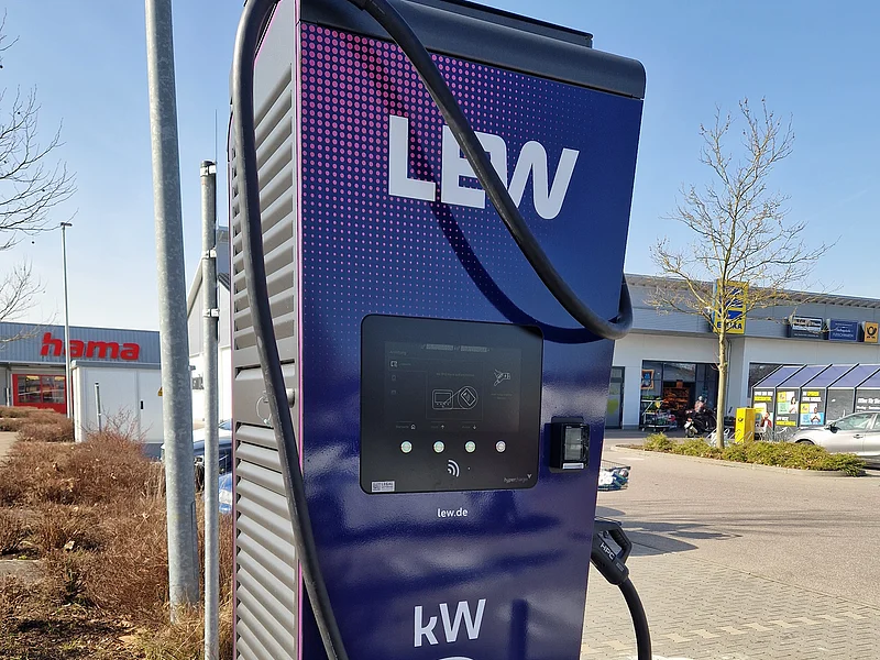Ladesäule für E-Autos mit einer Leistung von max. 400 kW Dunkle Ladestation für Elektroautos mit Anzeige auf Display und Kabeln zum Aufladen, im Freien auf einem Parkplatz vor Einkaufsgeschäften, bei Sonnenschein.