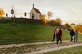 Vier Personen spazieren auf einem Weg an einer kleinen Kapelle vorbei, der Kalvarienbergkapelle in Wittesheim, umgeben von herbstlicher Landschaft. Auf dem Weg vor der Kapelle stehen Kreuzwegstationen.