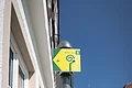Drei leuchtend gelbe Schilder am grauen Pfosten in einer Altstadt bei blauem Himmel. Zwei Schilder zu Wanderwegen mit der Nummern 5 und 6 und ein Pilgerweg-Symbol für den Wallfahrerweg, mit dem dazugehörigen spiralförmigen Symbol.