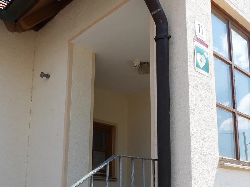 Eingang zu einem Feuerwehrhaus mit Treppe, Metallgeländer, Fenster und grünem Defibrillator-Schild an der Hauswand mit Hausnummer 11.
