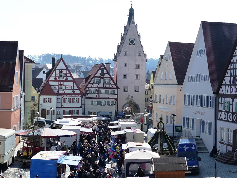 Herzlich Willkommen beim Josefsmarkt in Monheim Josefsmarkt in Monheim in der Altstadt: auf dem Marktplatz entlang Fachwerkhäuser, ein Turm mit Uhr und Menschenmengen zwischen vielen Marktständen bei Tageslicht.